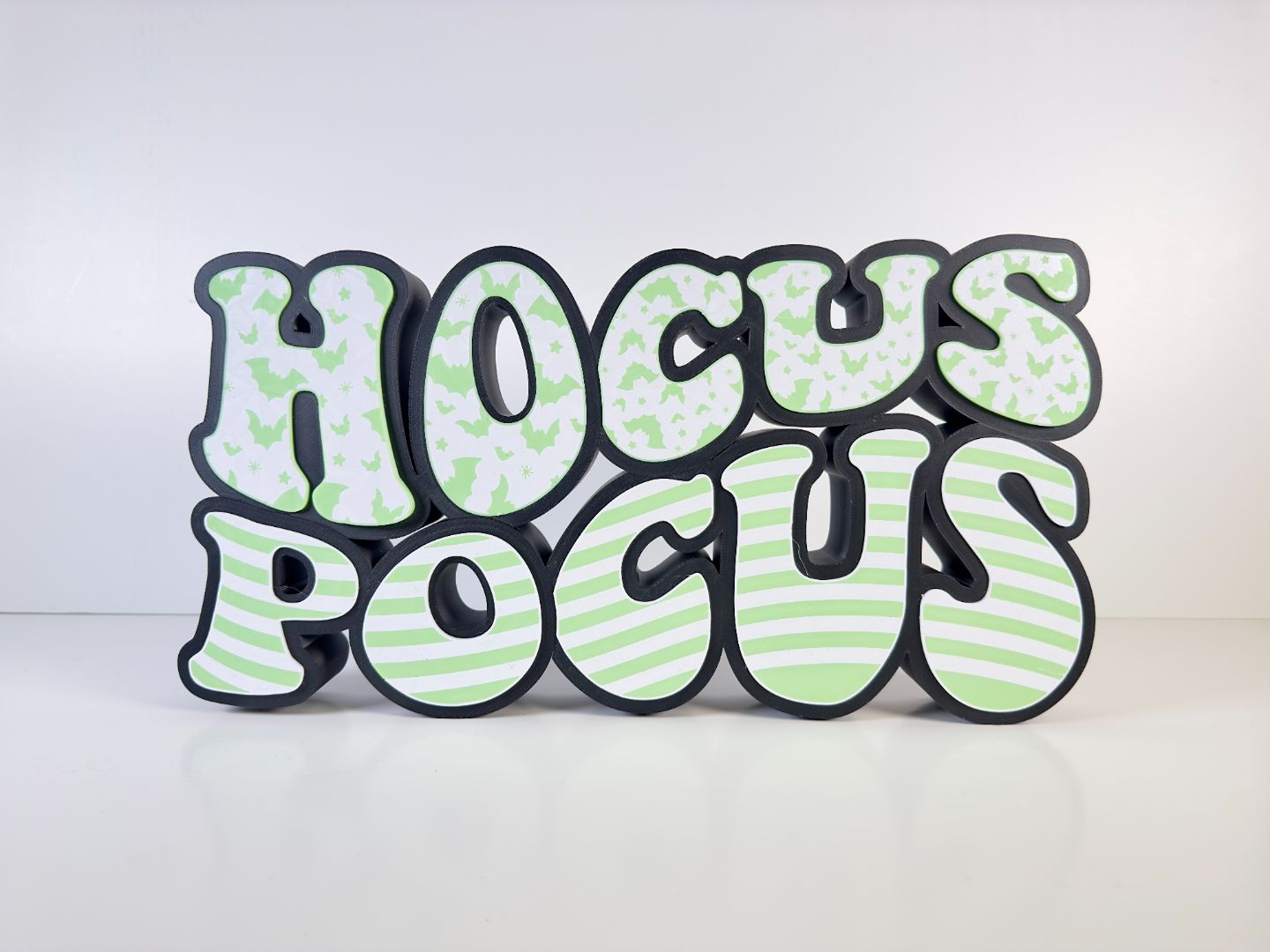Front view of a glowing “Hocus Pocus” LED sign featuring green bat patterns and stripes, set against a white background
