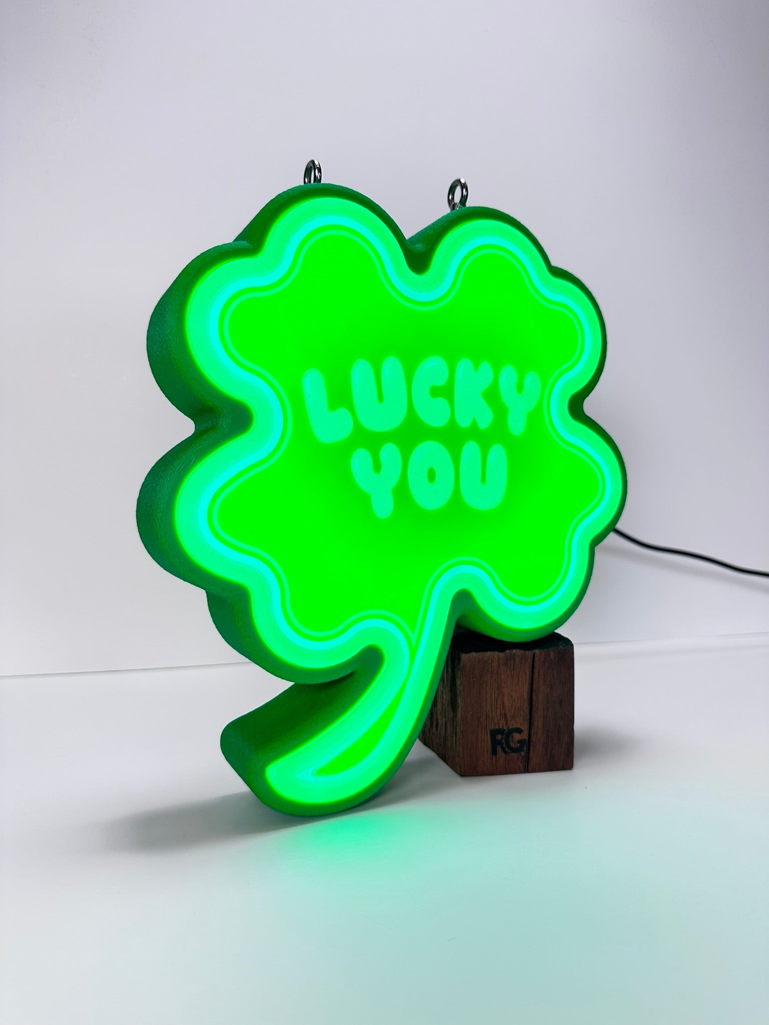 Angled view of the Shamrock LED sign, lit up with a vibrant green glow, sitting on a wooden stand