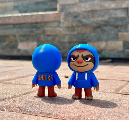 Two toy figures, one with a blue hood and 'Knicks' text, the other with a face, on a stone surface.