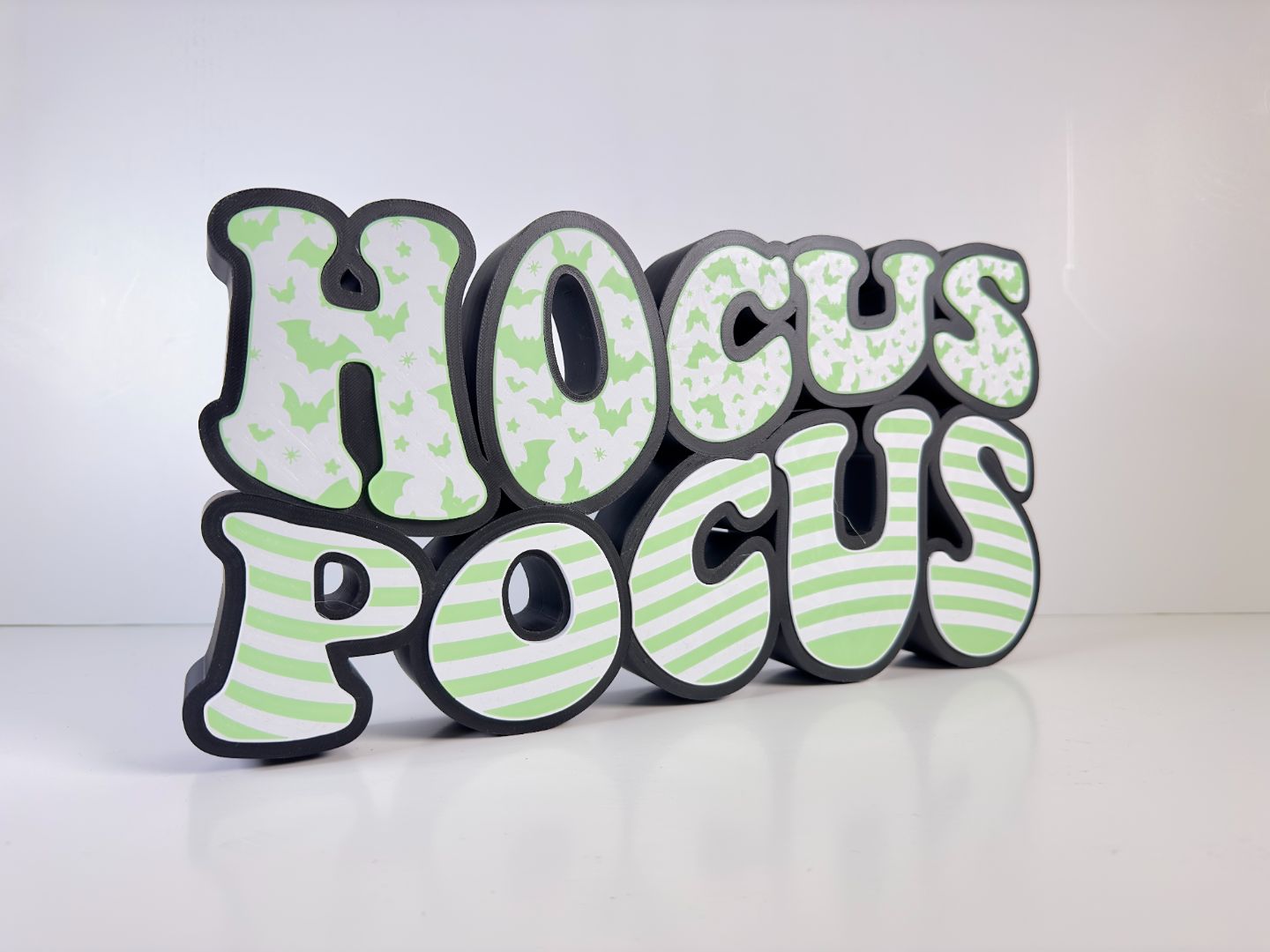 Side view of a “Hocus Pocus” LED sign with bat and stripe patterns, glowing with green LED lights, displayed on a white background.