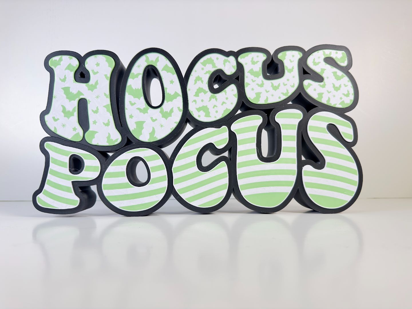 The “Hocus Pocus” LED sign glowing in the dark, with the bat patterns and striped letters illuminated in vibrant green