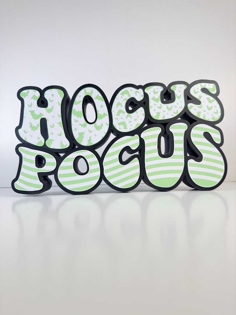 A glowing “Hocus Pocus” LED sign lighting up in the dark, with bold, whimsical text and bat patterns