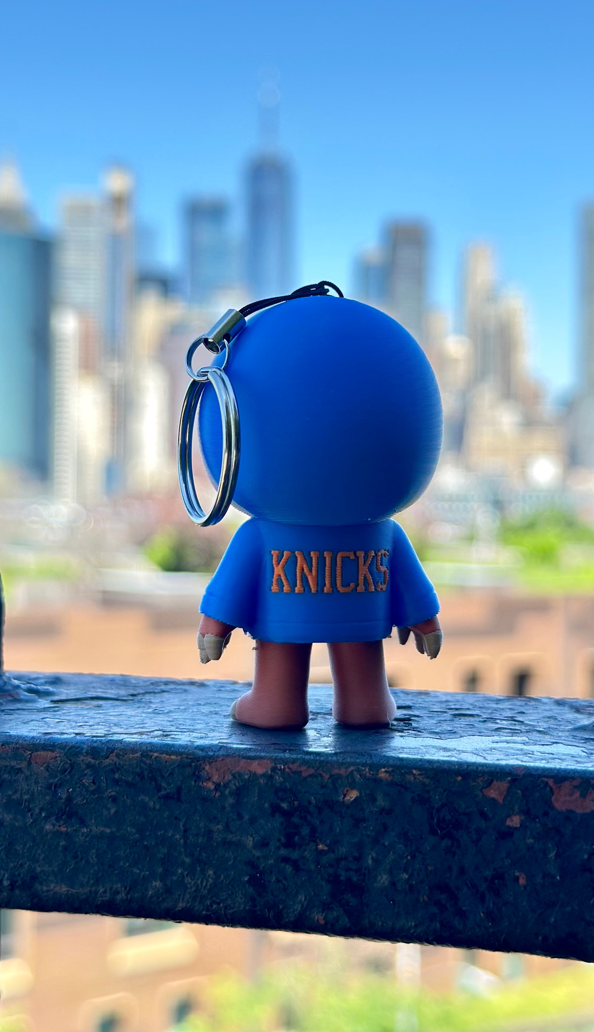 Blue 'Knicks' keychain figure with a city skyline in the background