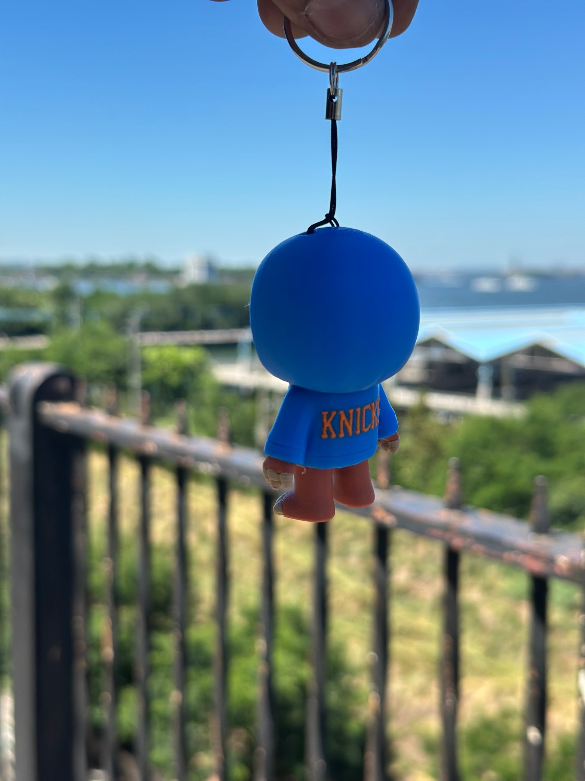 Blue ball with a keychain and 'knicks' tag held against a blurred outdoor background