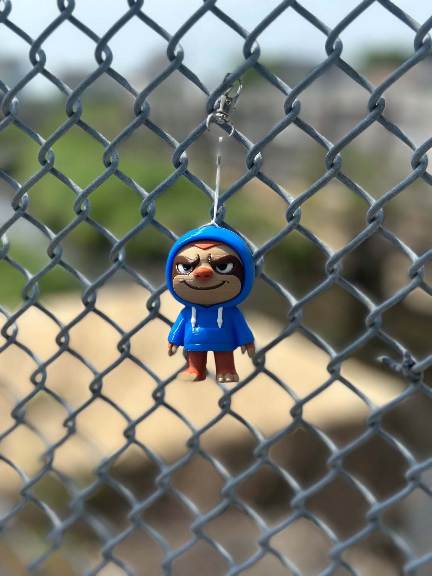 Keychain with a character in a blue coat hanging on a chain-link fence.
