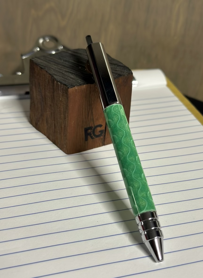 Green pen with silver accents on lined paper, next to a wooden block.