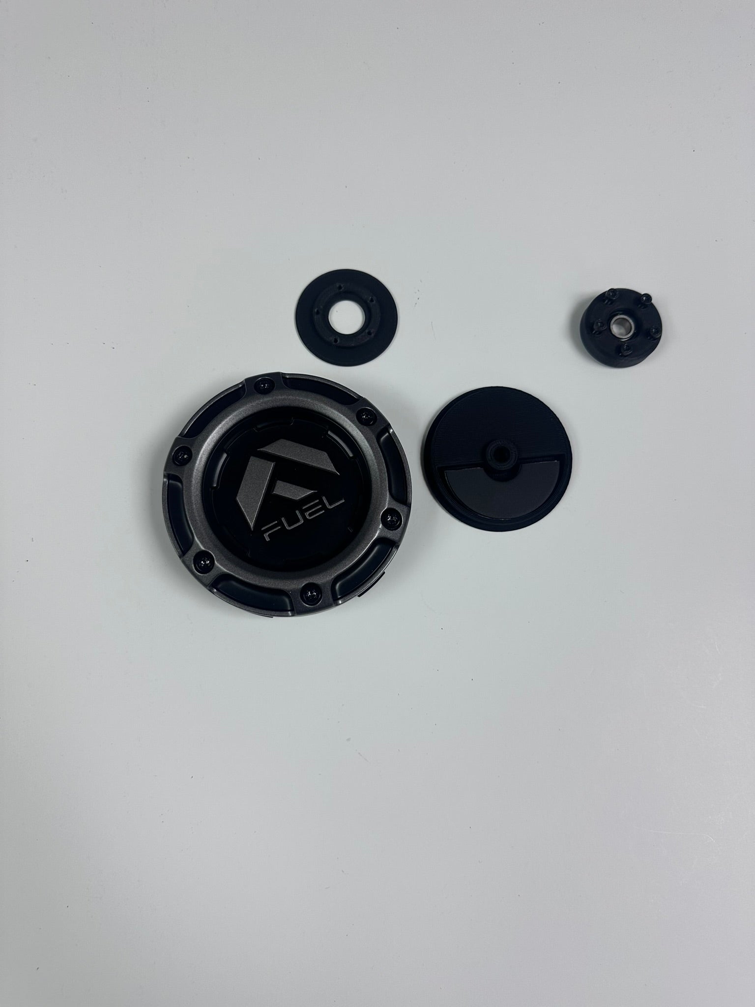 Components of the Fuel Wheel Floating Center Cap laid out on a white background, including the main cap, bearing, and weight.