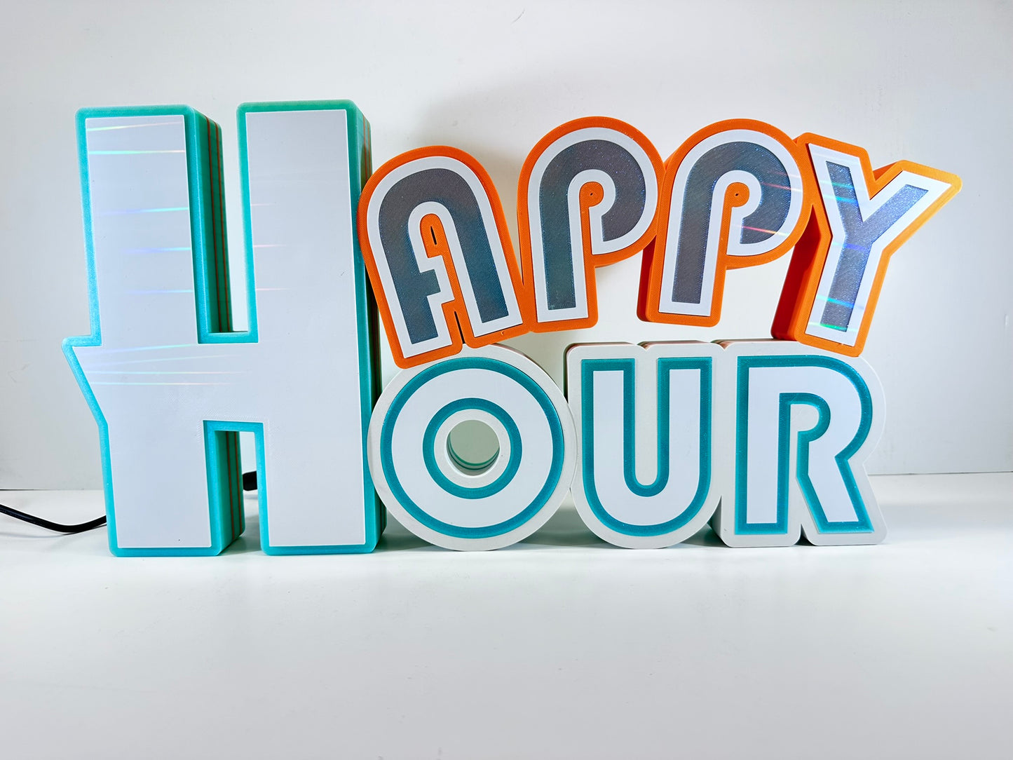 Front view of a 3D printed 'Happy Hour' sign under ambient light, emphasizing the clean, colorful design with turquoise and orange trim.