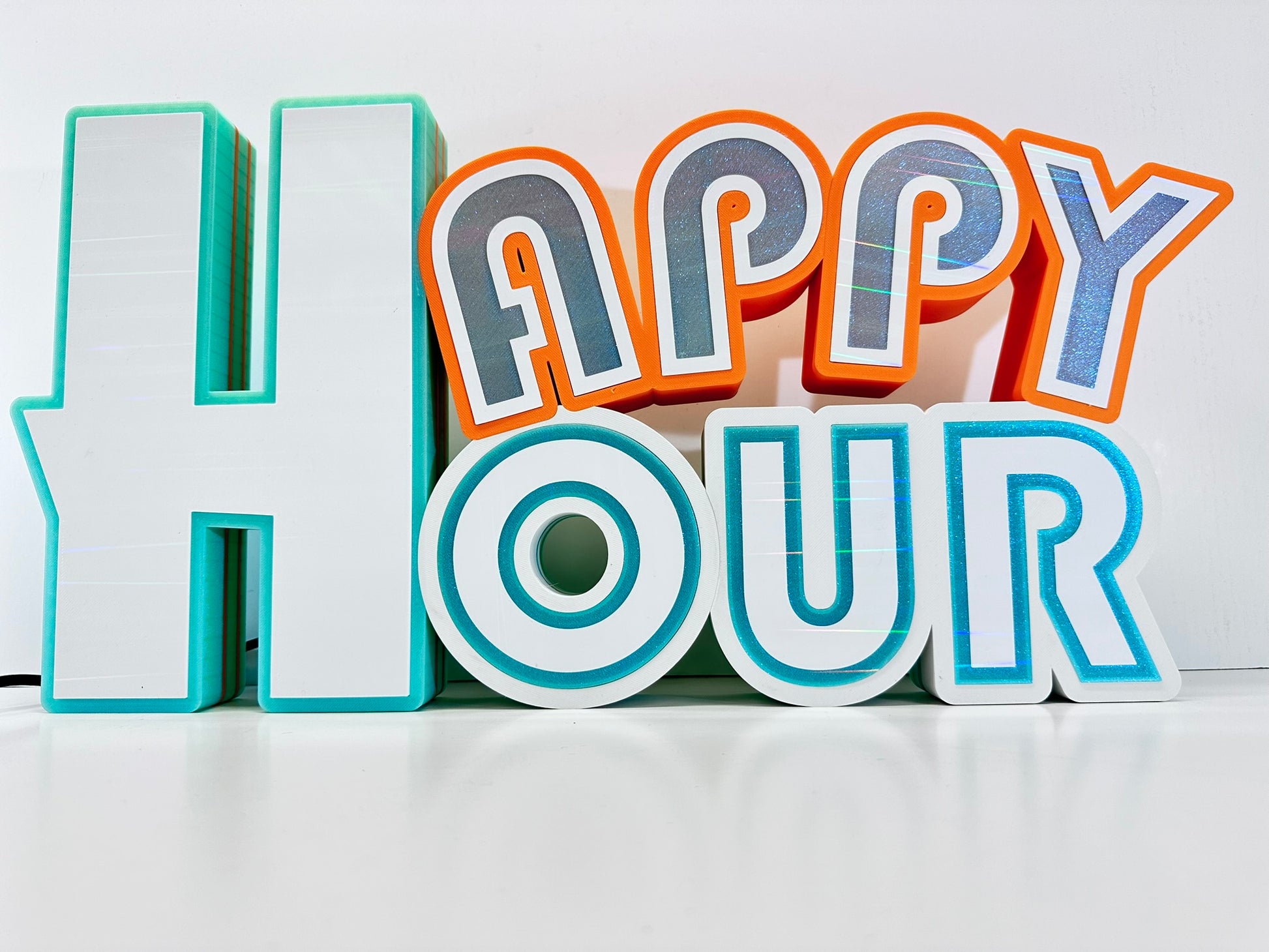 traight-on view of a 'Happy Hour' sign in 3D printed letters, with turquoise and orange accents, lit with vibrant LED colors