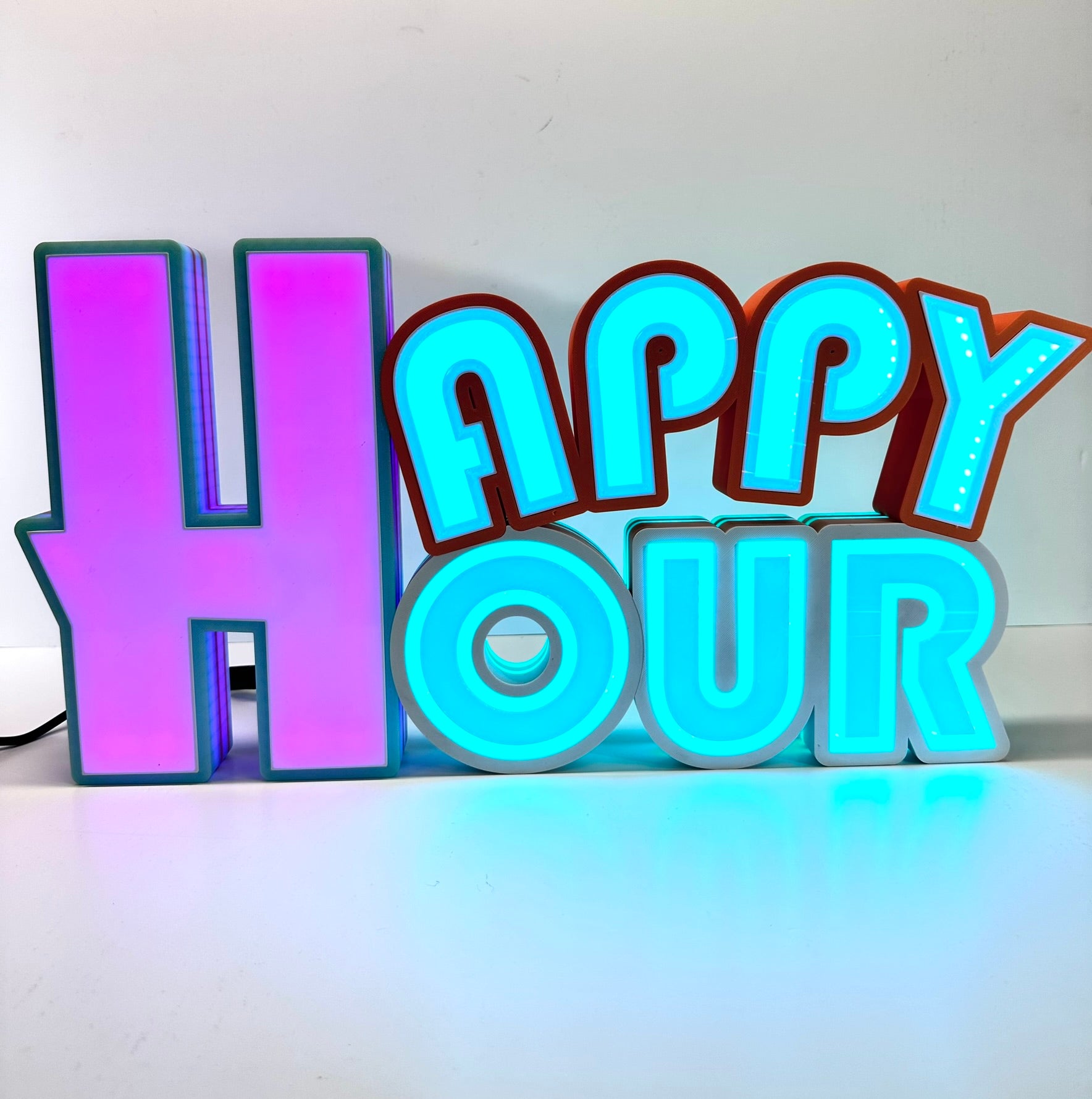 Straight-on view of a 'Happy Hour' sign in 3D printed letters, with turquoise and orange accents, lit with vibrant LED colors