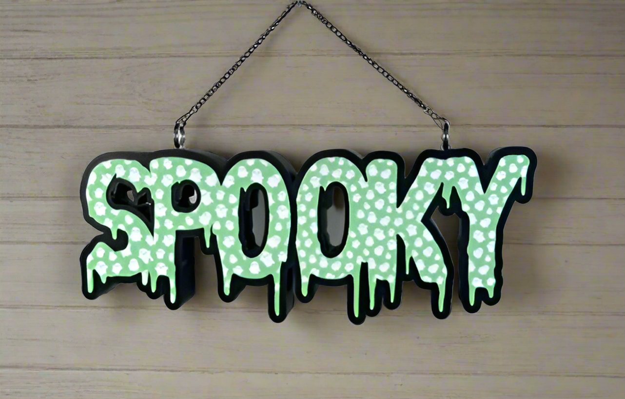 A “Spooky” LED sign with a dripping design, hanging from a chain. The letters are in green with mini ghost patterns, giving a fun and eerie Halloween vibe