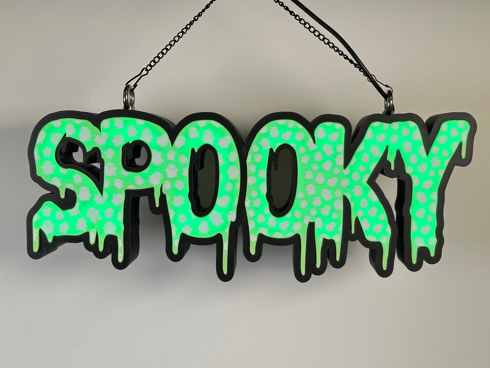 A glowing green “Spooky” LED sign against a white wall. The ghost patterns are illuminated, creating a spooky yet fun Halloween look