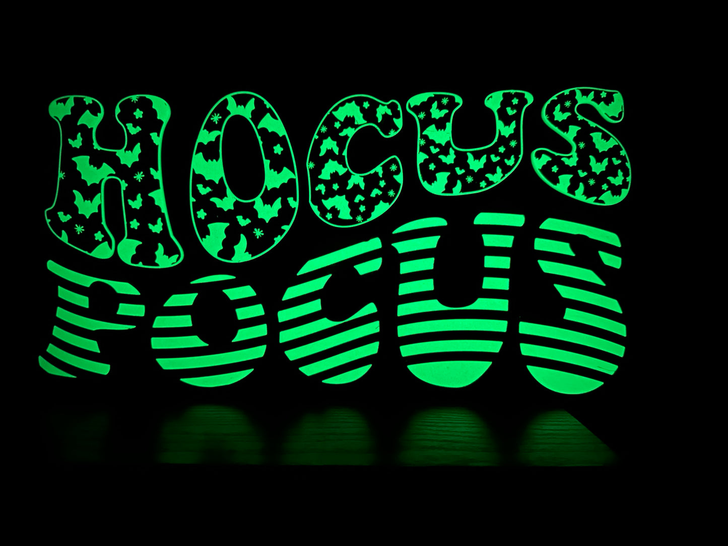 A “Hocus Pocus” LED sign resting on a flat white surface, with bold, glowing letters showcasing bat and stripe designs.