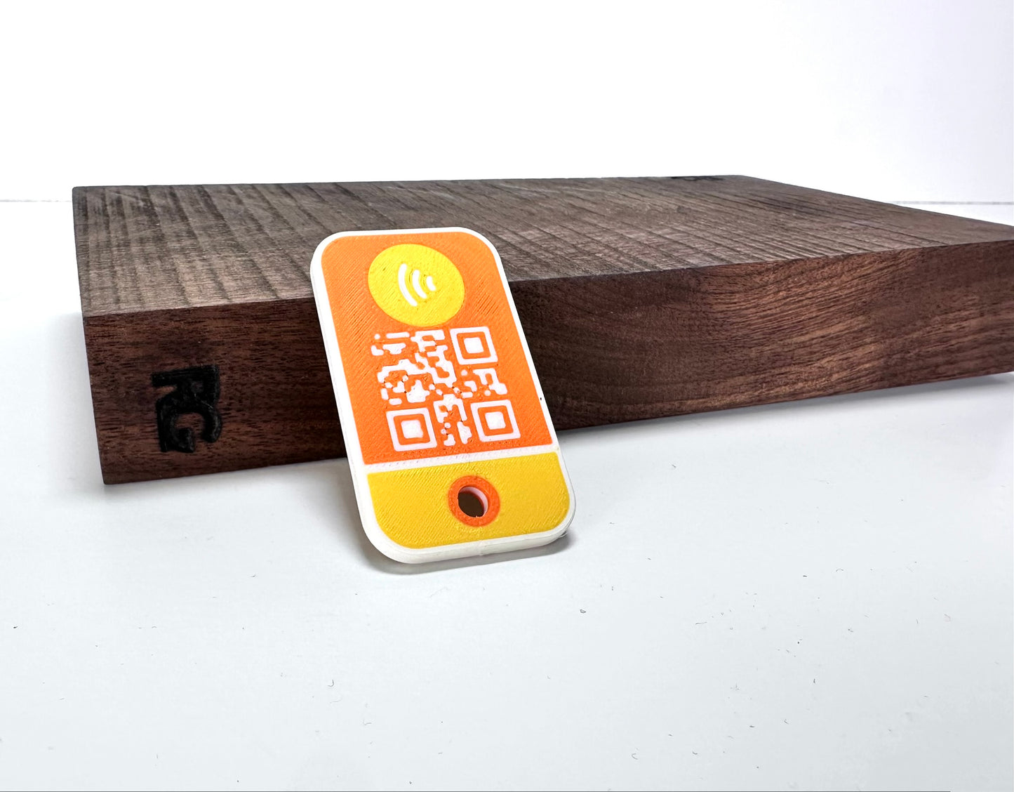 Reverse side of the yellow NFC/QR tag showing the QR code and NFC icon on a wooden stand with RG branding