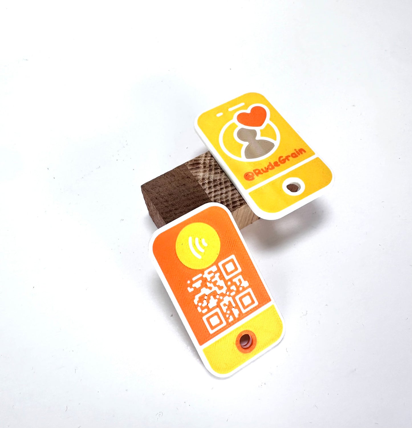 Yellow and orange NFC/QR tags angled on a wooden block, showcasing the front and back designs.