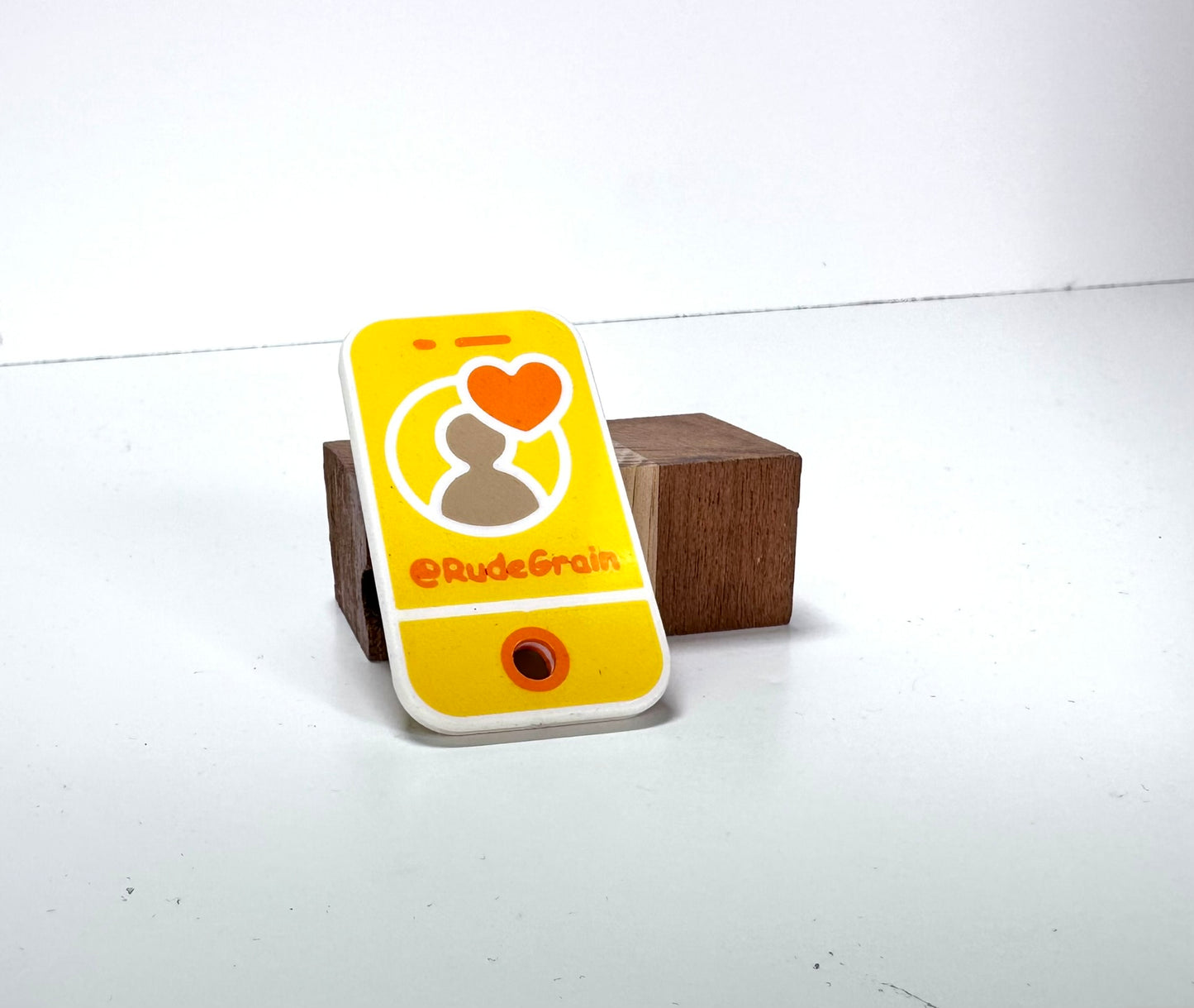 Yellow NFC/QR tag with a heart icon and @RudeGrain branding, placed on a clean white surface."