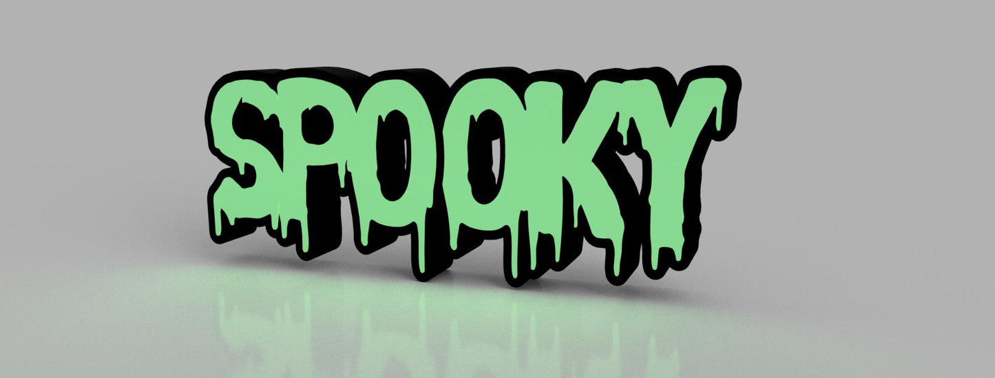 A side view of a “Spooky” sign with a dripping text design, filled with green color and outlined in black, resting on a reflective surface against a neutral background